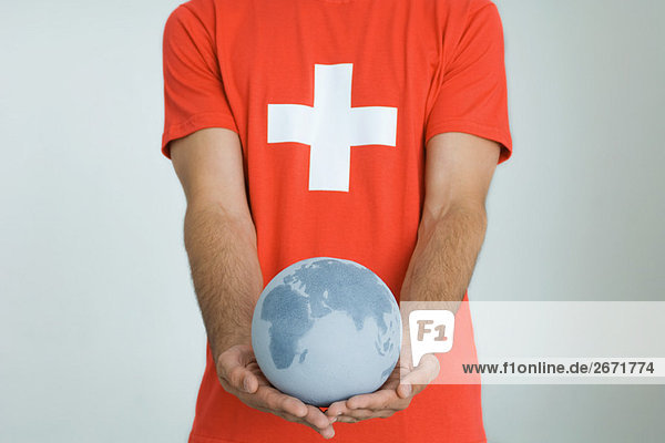 Mann im T-Shirt mit Schweizer Fahne  hält den Globus mit beiden Händen.