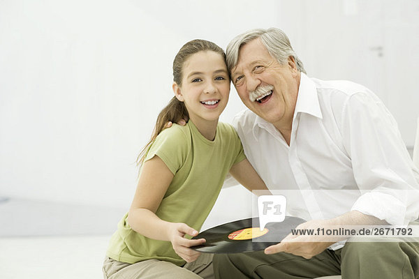 Grandfather and granddaughter holding record album together  smiling  portrait