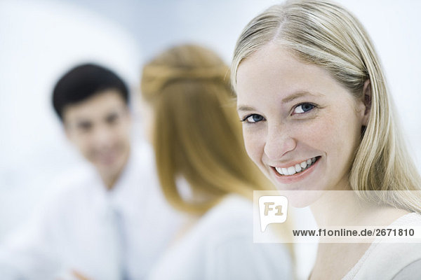 Young professional woman smiling at camera  colleagues talking in background