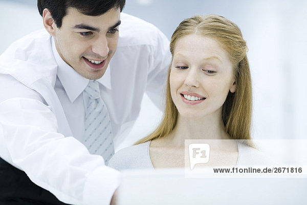 Professional man looking over female colleague's shoulder  pointing at laptop computer