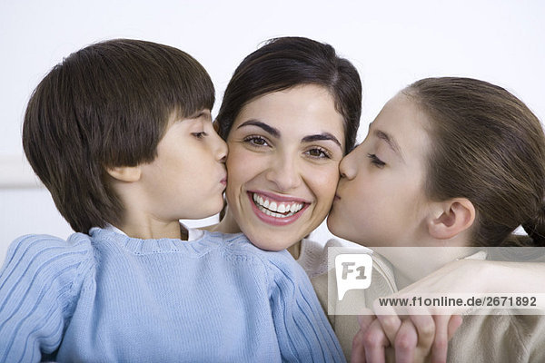 Portrait of smiling mother being kissed on each cheek by daughter and son