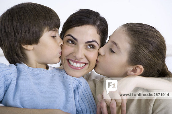 Portrait of smiling mother being kissed on each cheek by young daughter and son