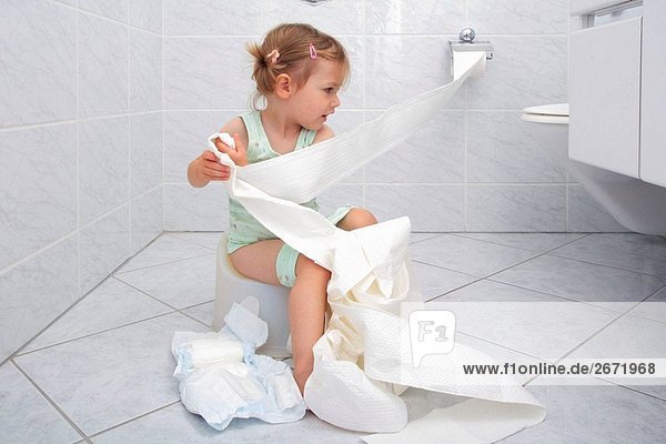Kleine Mädchen sitzen auf Töpfchen im Bad  während potty training  spielen und herumalbern Bandabroll WC-Papier