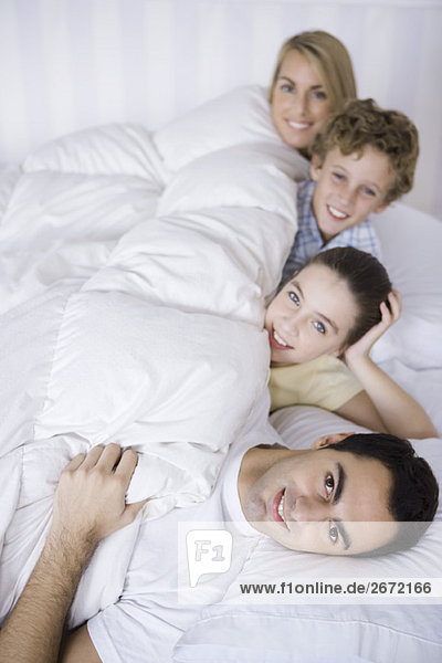 Family lying in bed together  smiling at camera