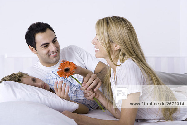 Family relaxing together on bed  woman holding flower