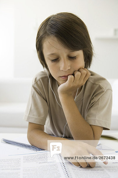 Junge liest Hausaufgaben und hört Kopfhörer