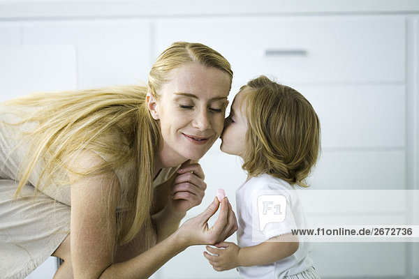 Kleines Mädchen küsst die Wange der Mutter  Frau hält ein winziges Herz  Augen geschlossen