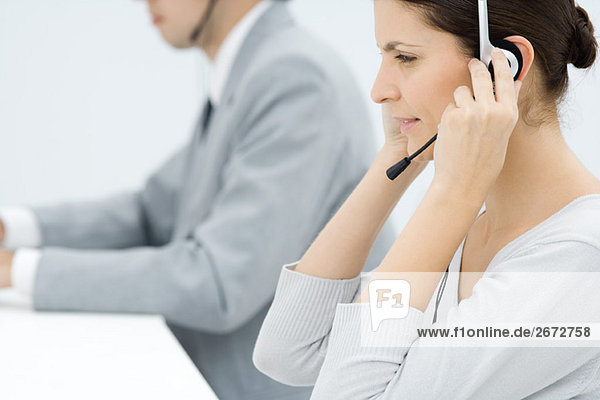 Professionelle Frau beim Einstellen des Headsets  männlicher Kollege im Hintergrund  Seitenansicht