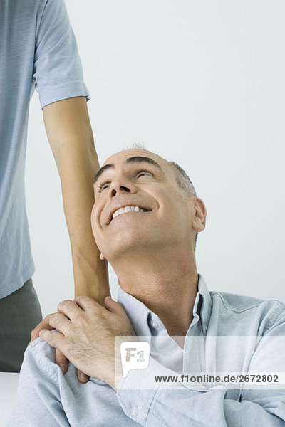 Der reife Mann hält die Hand des Sohnes auf der Schulter  lächelt über die Schulter  Blick in den Ausschnitt