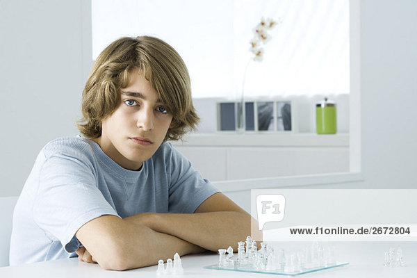 Jugendlicher Junge sitzt am Tisch  spielt Schach  schaut in die Kamera