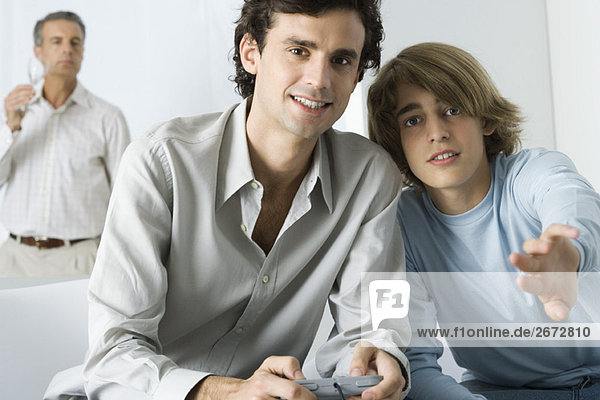 Young man and teen brother playing video game  looking at camera