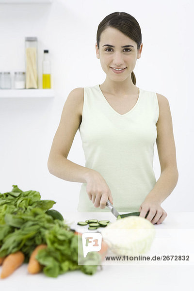 Woman slicing cucumber  assorted vegetables in foreground  smiling at camera