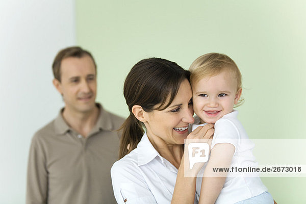 Woman holding up baby  husband standing in background