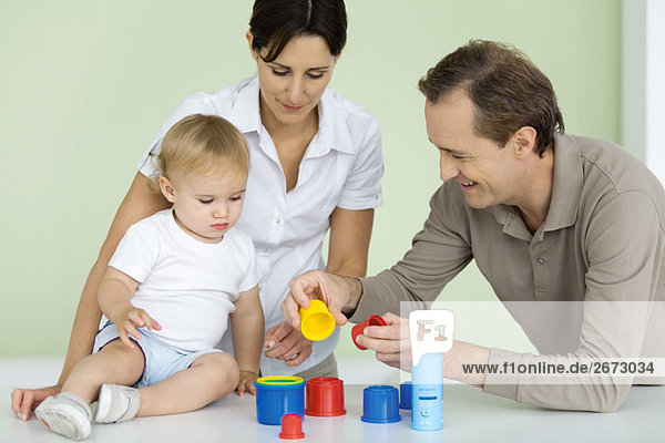 Father showing toddler plastic toys  mother watching