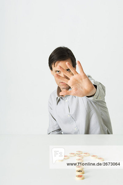 Mann mit offener Handfläche in Richtung Kamera  chinesische Schachfiguren in Form eines Pfeils auf ihn gerichtet