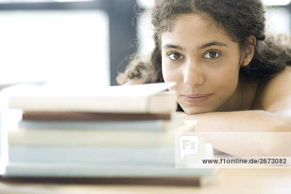 Young woman resting head on arms  behind pile of books