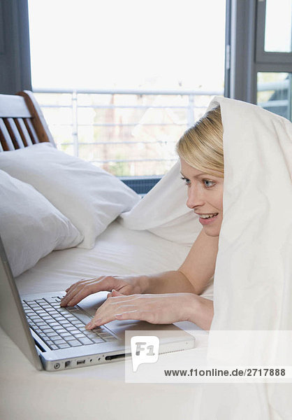 Frau bei der Arbeit am Laptop im Bett