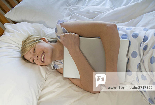 Weibliche Umarmung ihres Laptops im Bett