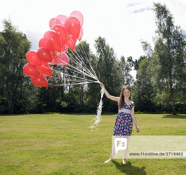 Girl holding bunch of red balloons