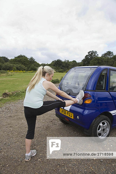 Young woman exercising by electric car