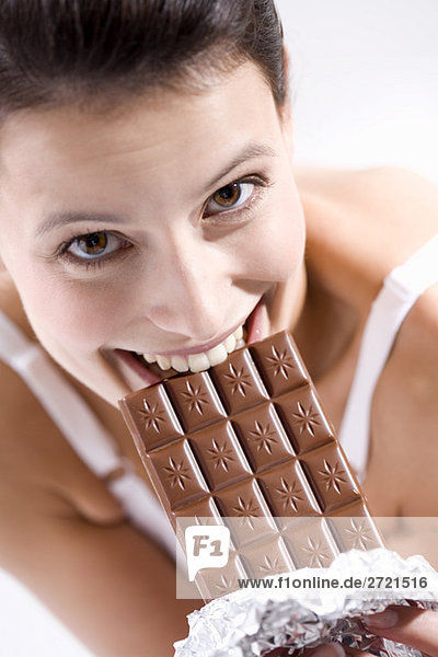Young woman biting into chocolate bar  smiling