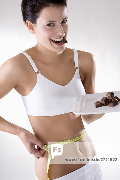 Junge Frau prüft ihre Taille mit Maßband  hält Schokolade auf Tablett