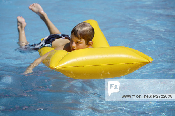 Junge (10-11 auf Luftmatratze im Pool liegend