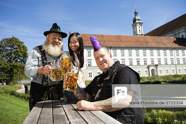 Deutschland  Bayern  Oberbayern  Drei Leute im Biergarten mit Bierkruggläsern  lächelnd