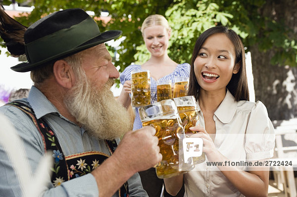 Upper   n man and Asian woman in beer garden raising stein glasses  portrait