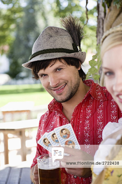 Upper   Young couple in beer garden  man holding playing cards