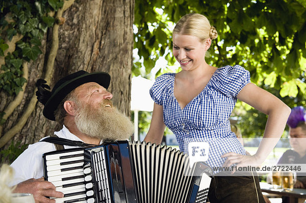 Upper   Senior man in traditional costume playing accordion in beer garden