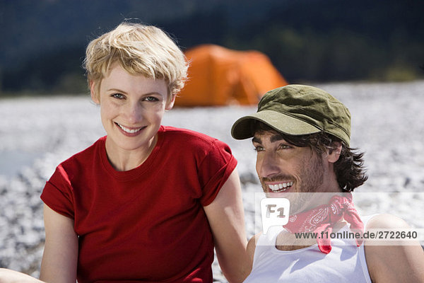 Deutschland  Bayern  Tölzer Land  Junges Paar am Fluss sitzend  Portrait  Nahaufnahme