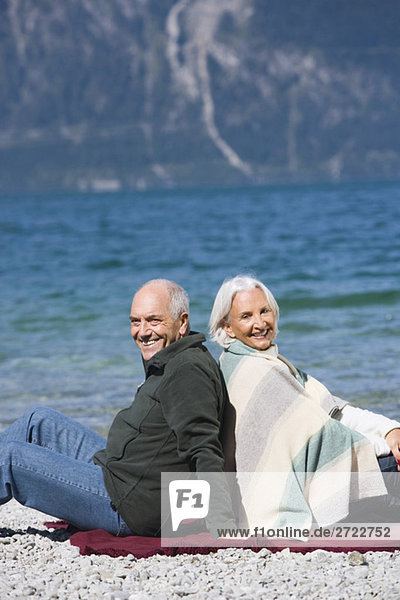 Germany  Bavaria  Senior couple relaxing on lakeshore  sitting back to back
