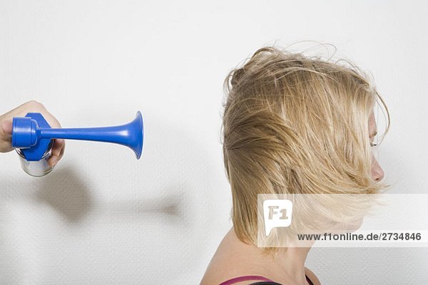 Eine Frau mit einem Lufthorn  das am Hinterkopf geblasen wird.