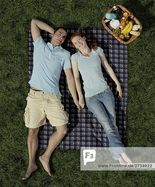 Ein junges Paar liegt auf einer Decke mit einem Wäschekorb.