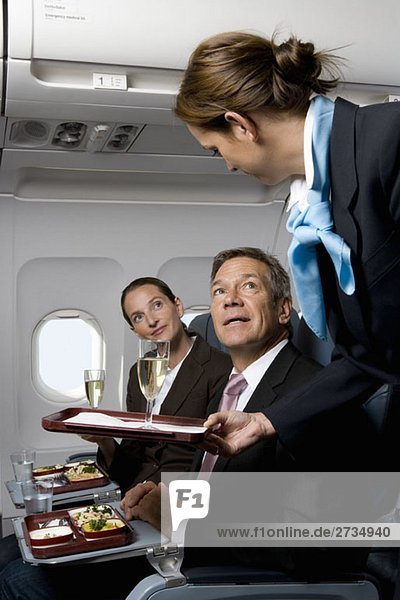 Geschäftsleute in einem Flugzeug  die Mahlzeiten und Champagner bekommen.