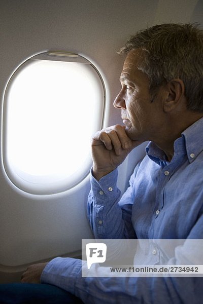 Ein männlicher Passagier in einem Flugzeug  der durchs Fenster schaut.