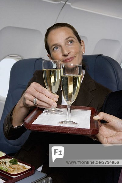 Eine Geschäftsfrau  der im Flugzeug Champagner serviert wird.