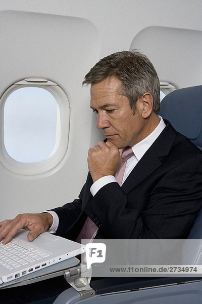 Ein Geschäftsmann  der einen Laptop in einem Flugzeug benutzt.