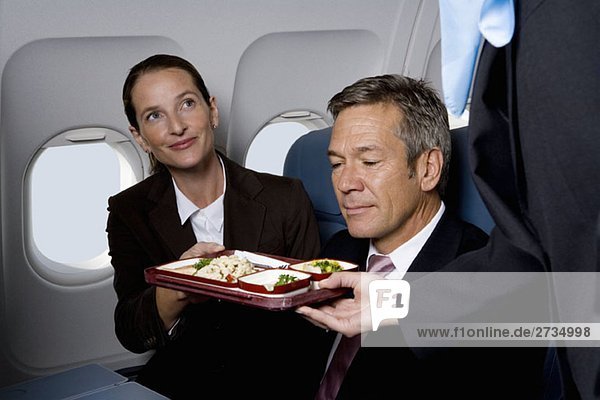 Geschäftsleute in einem Flugzeug  das mit Airline-Lebensmitteln versorgt wird.