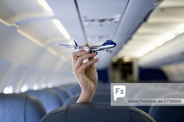 Eine Hand  die ein Spielzeugflugzeug über einem Flugzeugsitz hält.