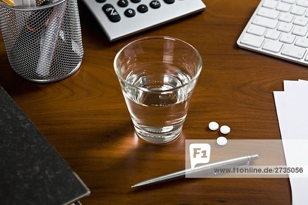 Ein Schreibtisch mit einem Stift und einem Glas Wasser mit drei Aspirin daneben.