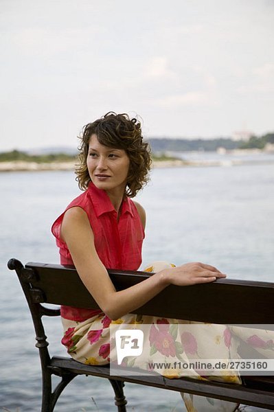 Eine Frau sitzt auf einer Bank am Meer.