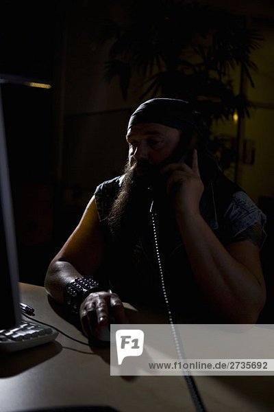 A biker sitting in a darkened office on the phone