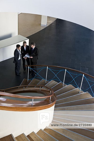 Drei Geschäftsleute  die am Fuße einer Treppe stehen.