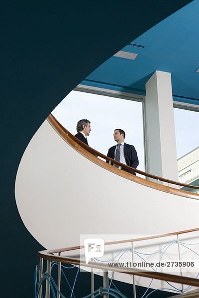 Zwei Geschäftsleute  die oben auf einer Treppe stehen und reden.
