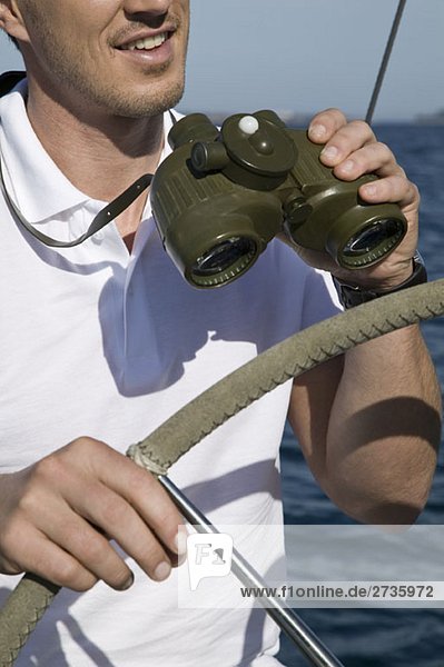 Detail eines Mannes mit Fernglas am Steuer einer Yacht