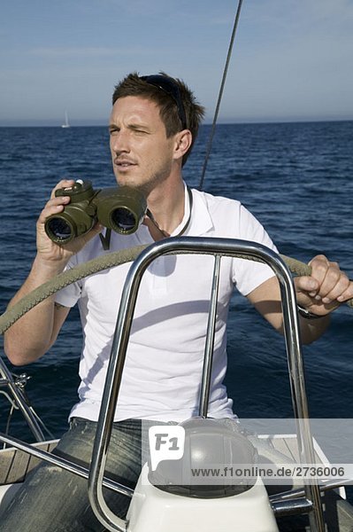 A man with binoculars at the helm of a yacht