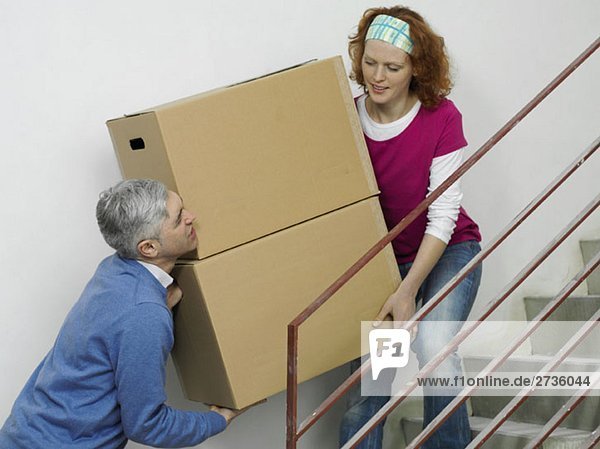 Ein Paar trägt Kisten zusammen die Treppe hinauf.