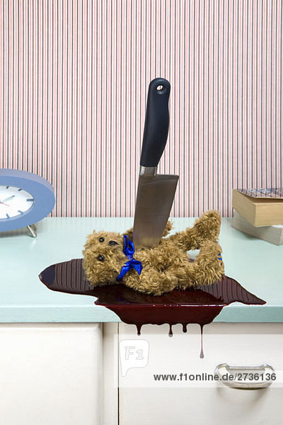 Messer  das einen Teddybären auf eine Kommode sticht.